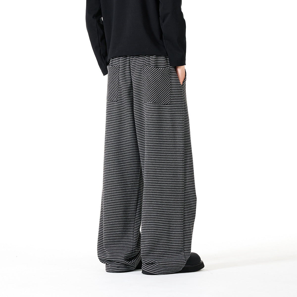 Back view of a model wearing dark wide-leg pants with thin white horizontal stripes and a plain black top.