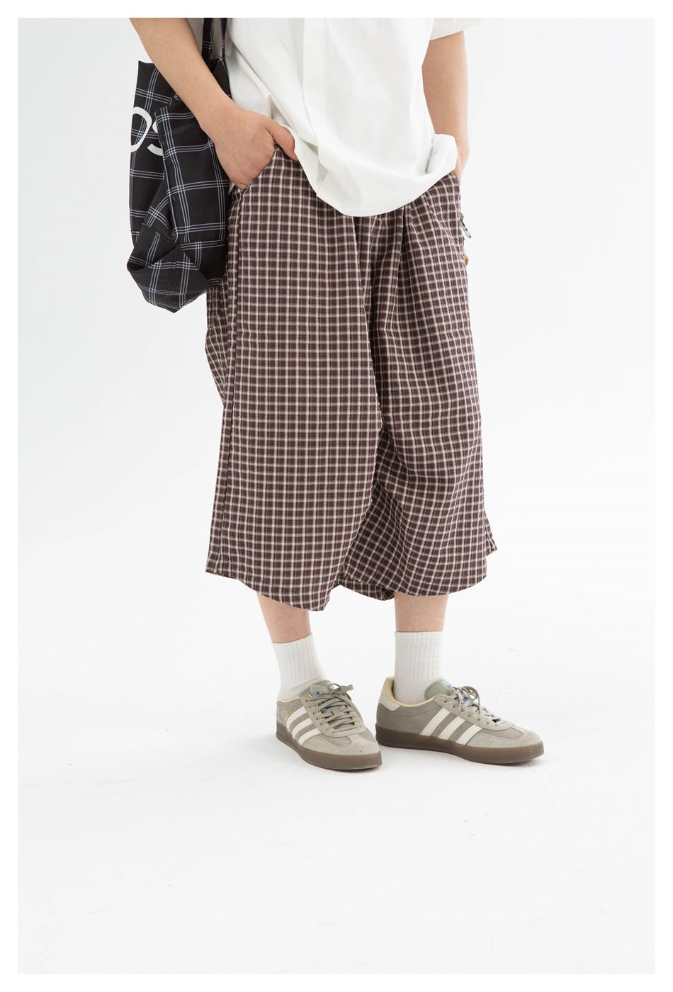 Close view of brown plaid knee-length shorts worn with a white shirt, showing the roomy legs and side pockets.