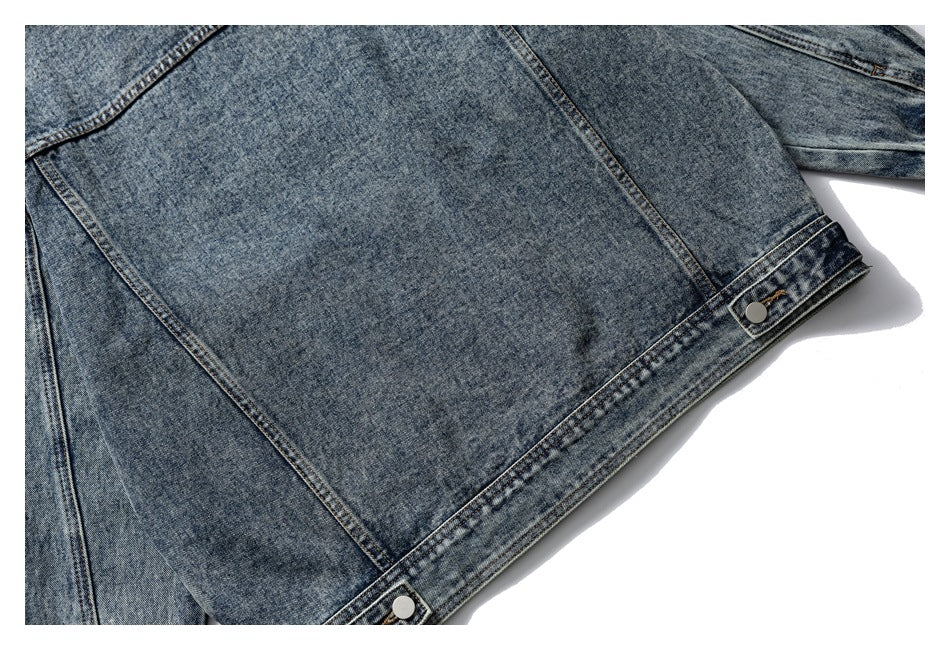 Partial flat-lay view of the back of a blue denim jacket, with panel seams and snap-fastened hem tabs.