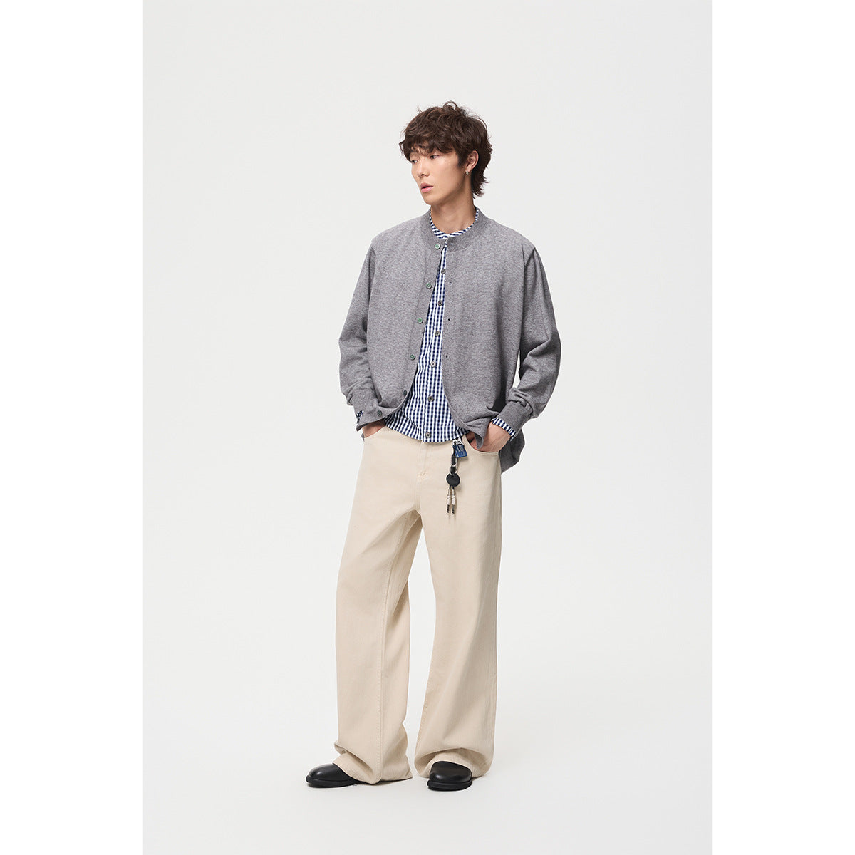 Model wearing a gray button-front cardigan over a blue checked shirt with loose cream trousers.
