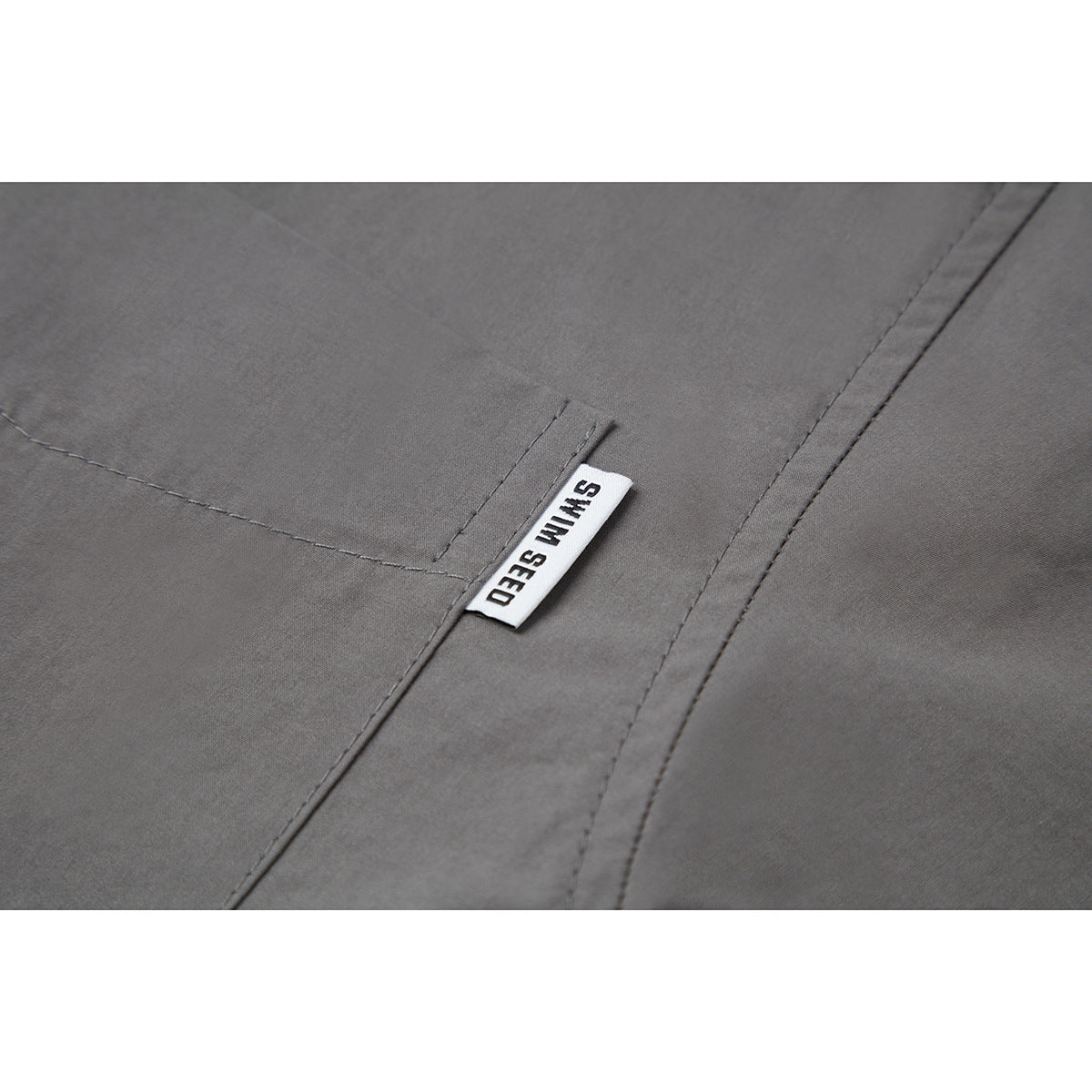 Close-up of gray shirt fabric, stitching, and a white SWIM SEED tab beside a seam.