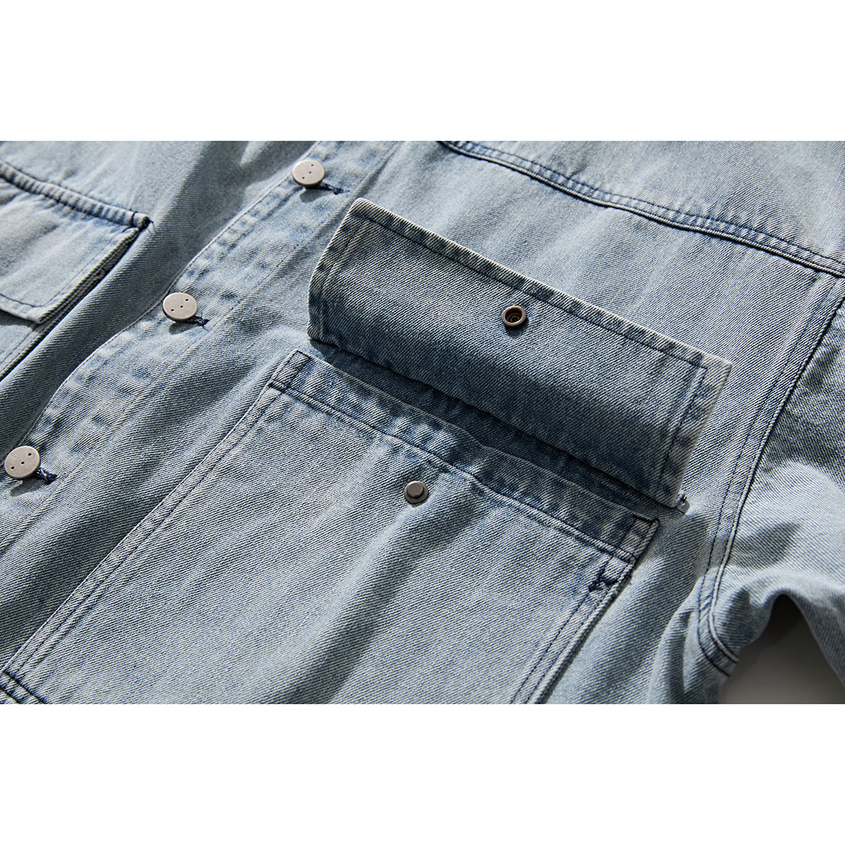 Close-up of a light blue washed denim jacket showing its button-front placket and large flap pockets.