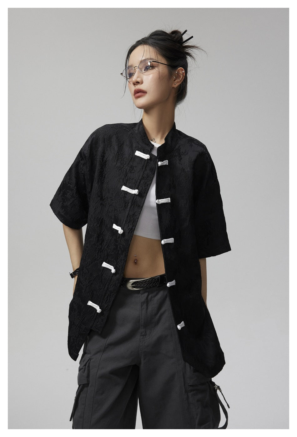 Model wearing an open black short-sleeve jacket with white frog closures over a white top.