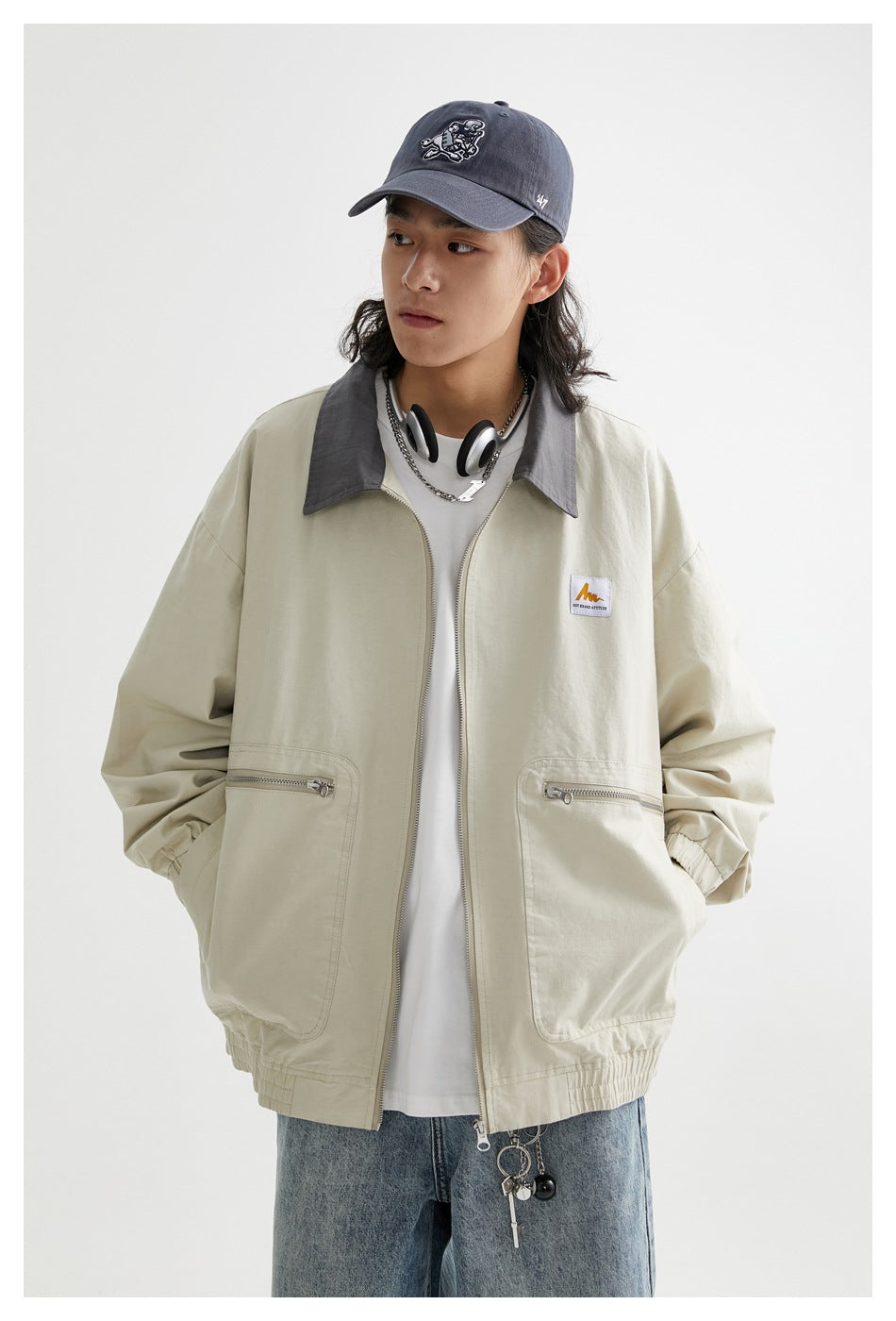 Front view of a model in a pale beige jacket with a gray collar, front zipper, elastic cuffs, and two zip pockets.
