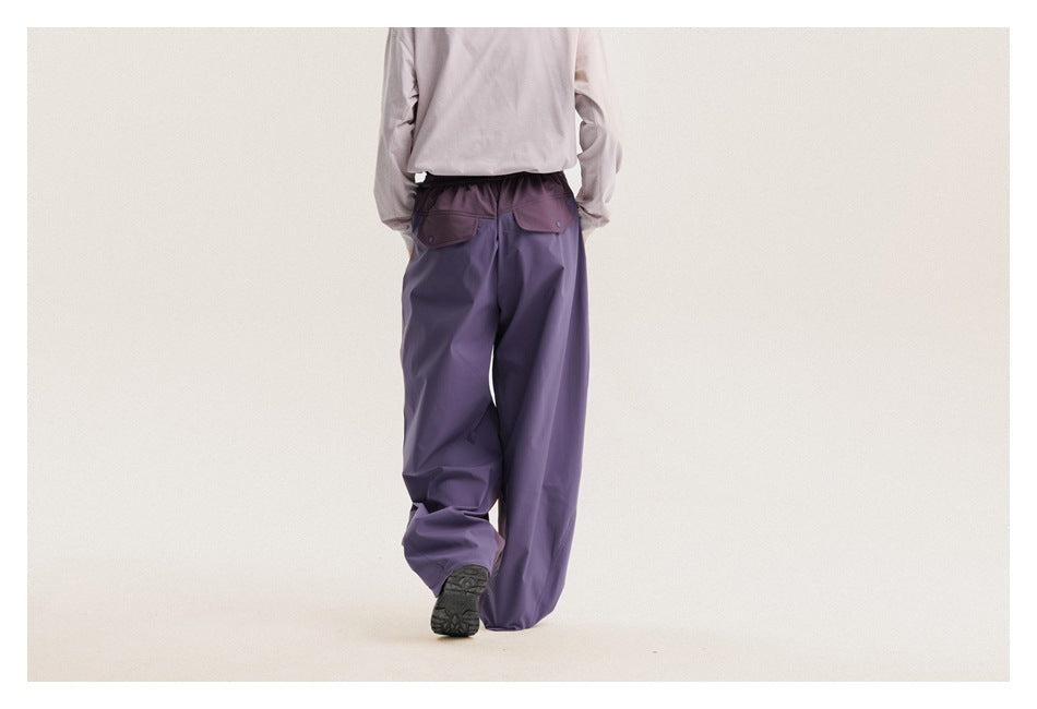 Back view of a model wearing loose purple pants with two flap pockets and an elastic waist.