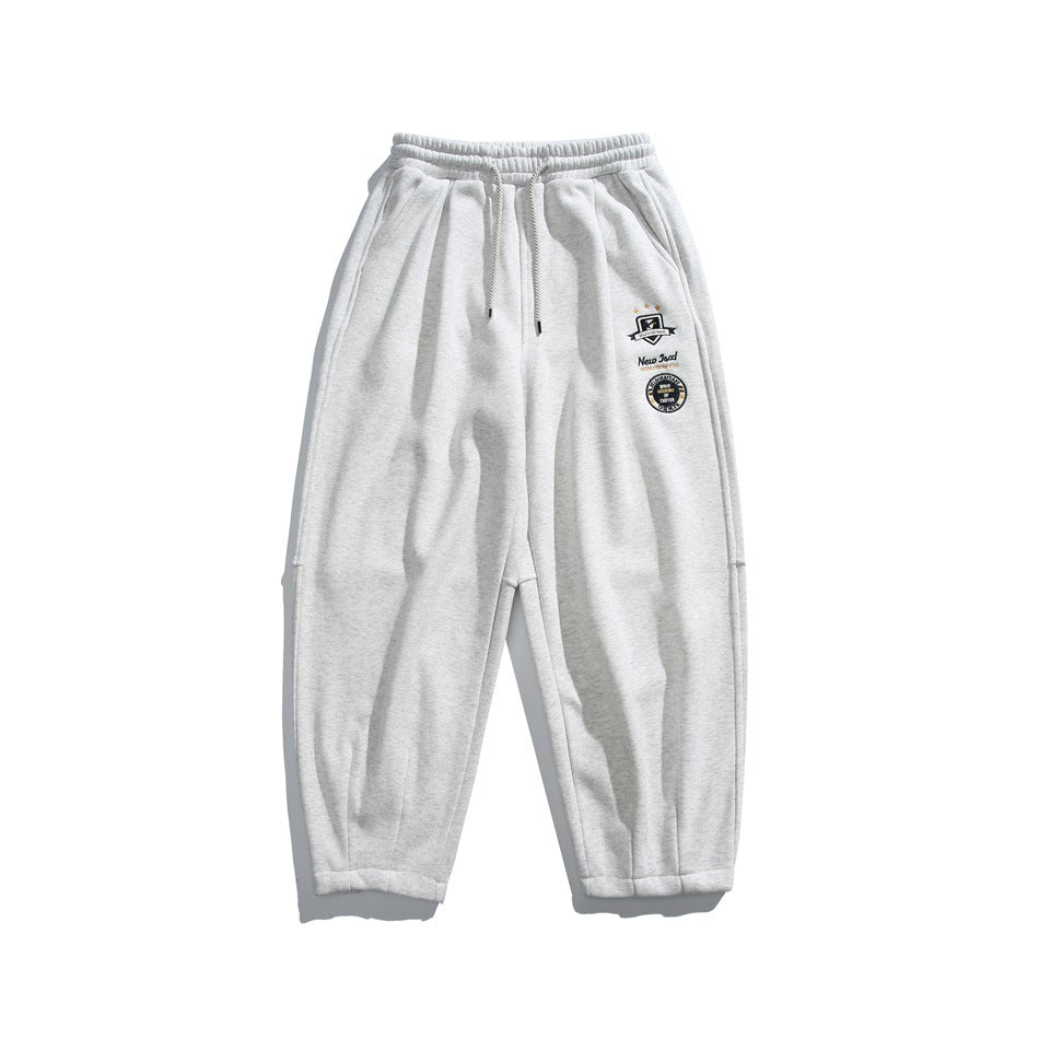 Heather gray sweatpants flat lay with drawstring waist, side pockets and embroidered badges on the left leg