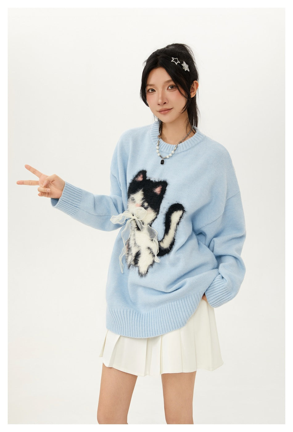 Model wearing a light blue oversized sweater with a fluffy cat applique and white pleated skirt.
