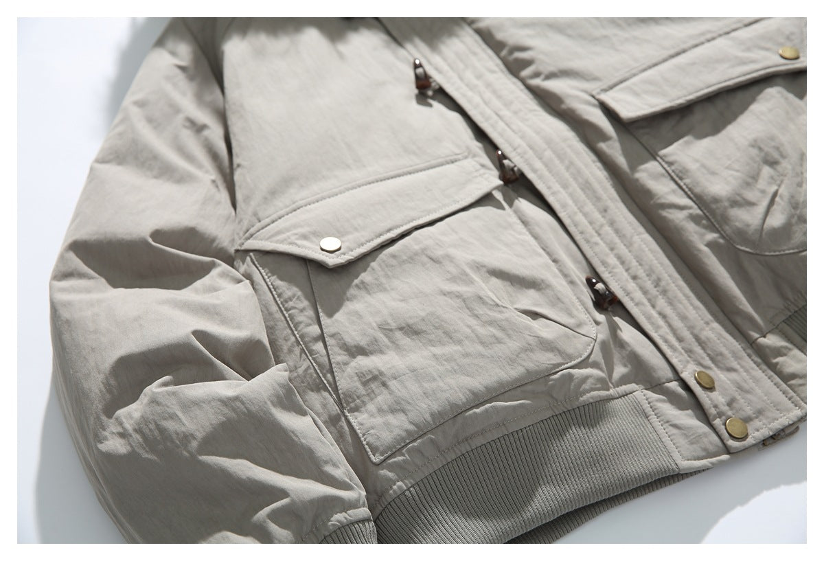 Close-up of a taupe jacket front with flap pockets, toggle fasteners, and a ribbed hem.