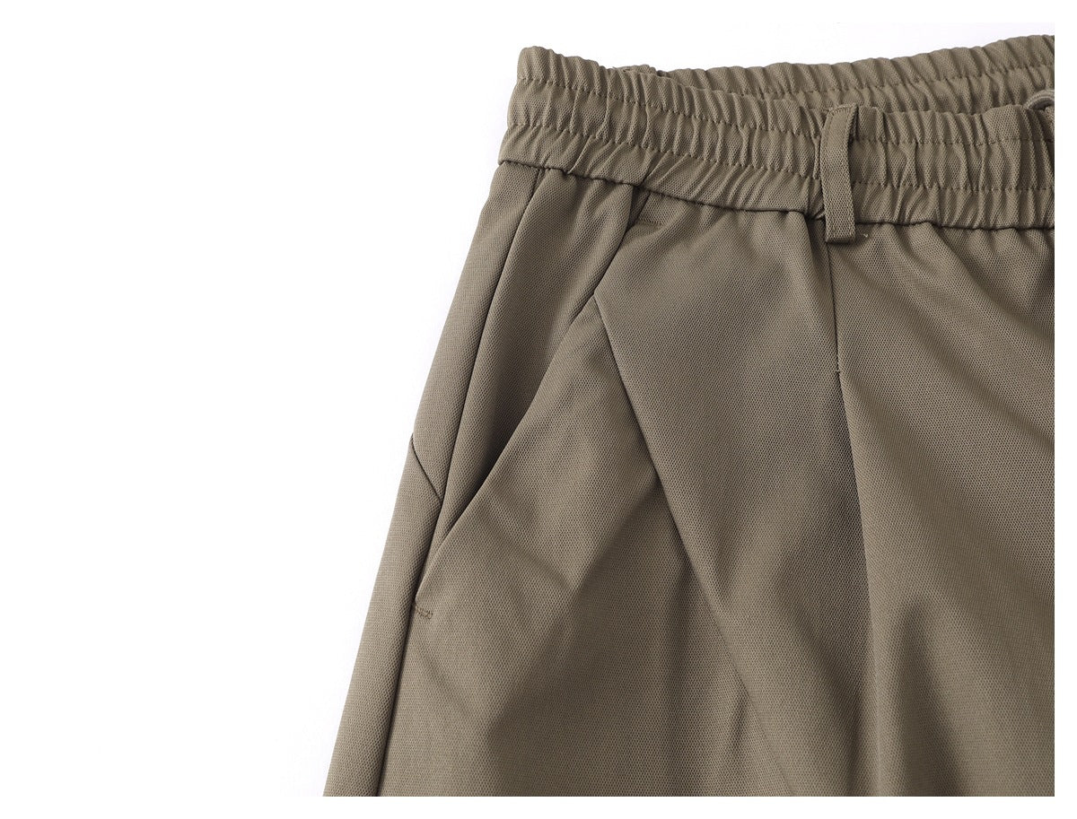 Close-up of taupe trousers showing the elastic waistband, belt loop, and curved front pocket seam.