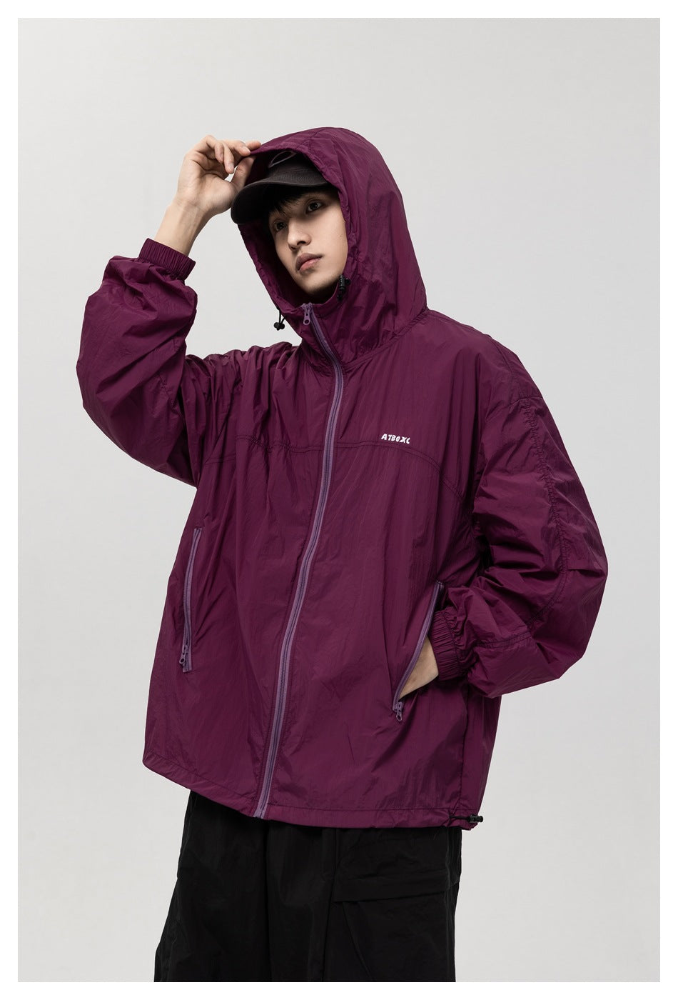 Model wearing a plum hooded jacket with the hood up, front zipper, and two zippered pockets.