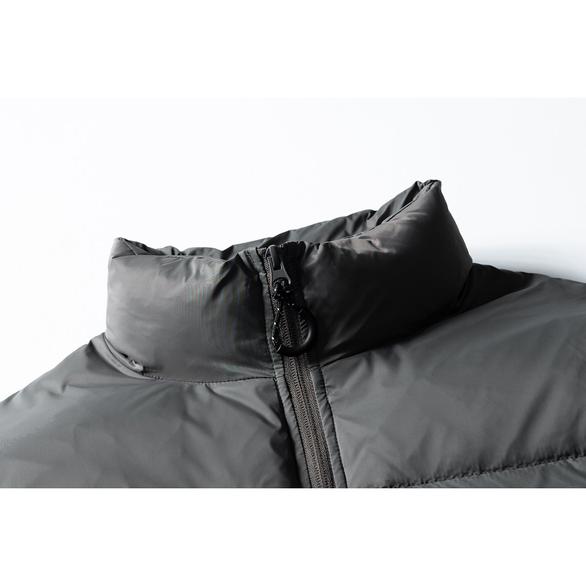Close-up of a charcoal puffer jacket's raised collar and front zipper with a large pull tab.