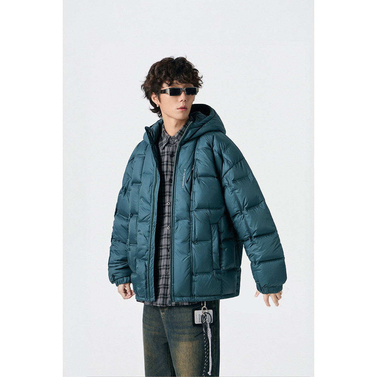 Model wearing a teal hooded puffer jacket over a plaid shirt, shown from the front.