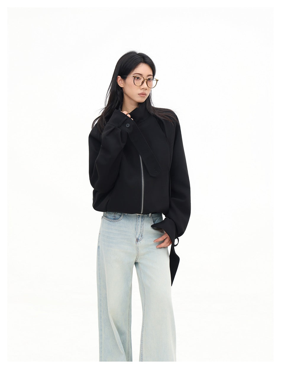 Model in a black jacket with a high collar, asymmetrical front detail, and silver zipper, styled with light-wash jeans.