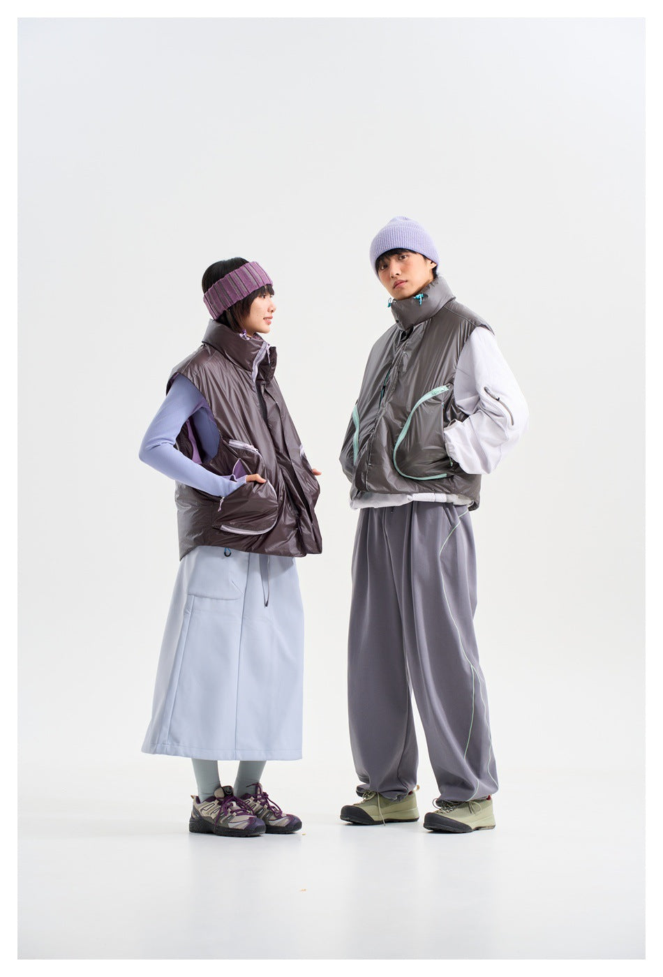 Two models in charcoal sleeveless vests shown at an angle, with contrasting pocket trim and coordinated outfits.