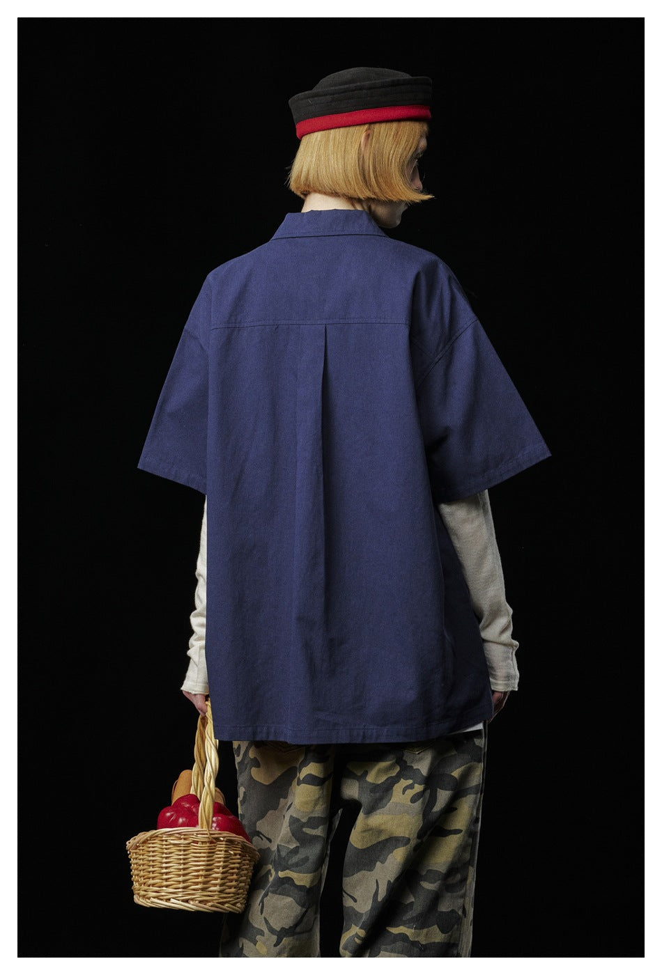Back view of a model wearing an oversized navy short-sleeve shirt over a cream long-sleeve top.