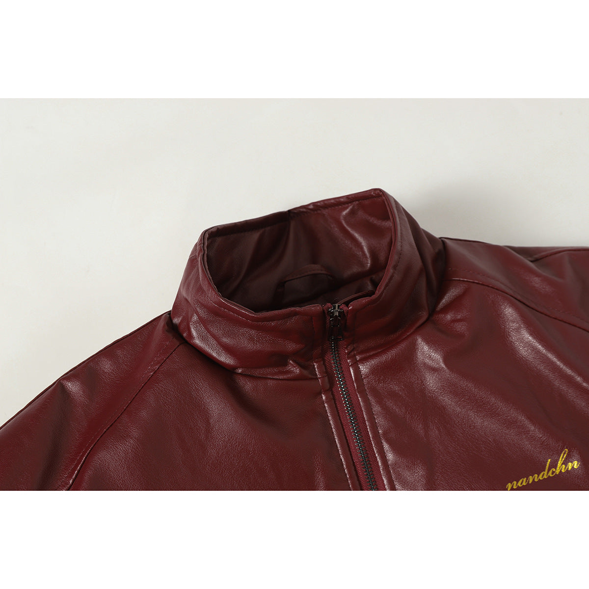 Close-up of a burgundy jacket's stand collar and front zipper, with small gold script embroidery.