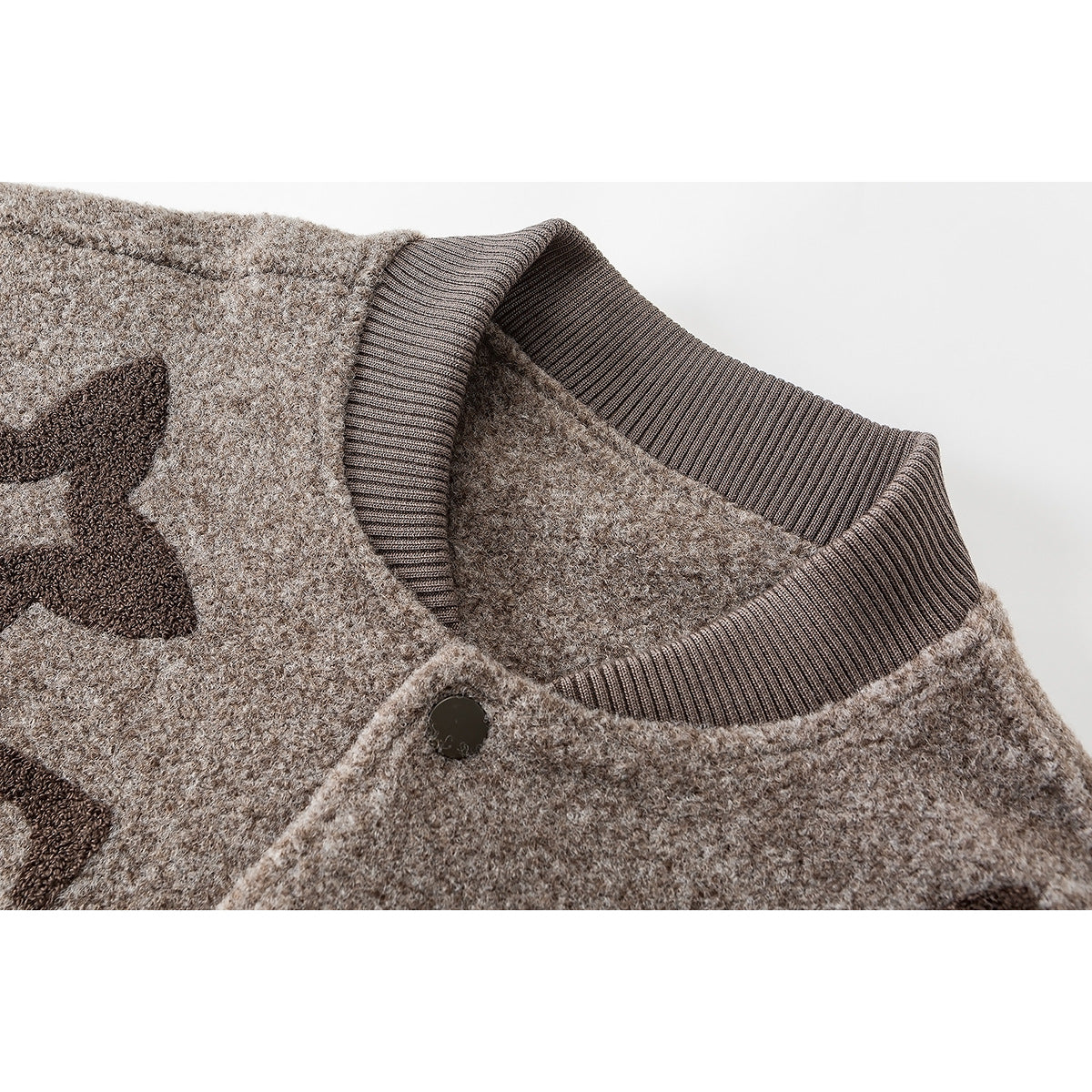 Close-up of a taupe varsity jacket's ribbed collar, snap button and textured fabric with dark motifs.