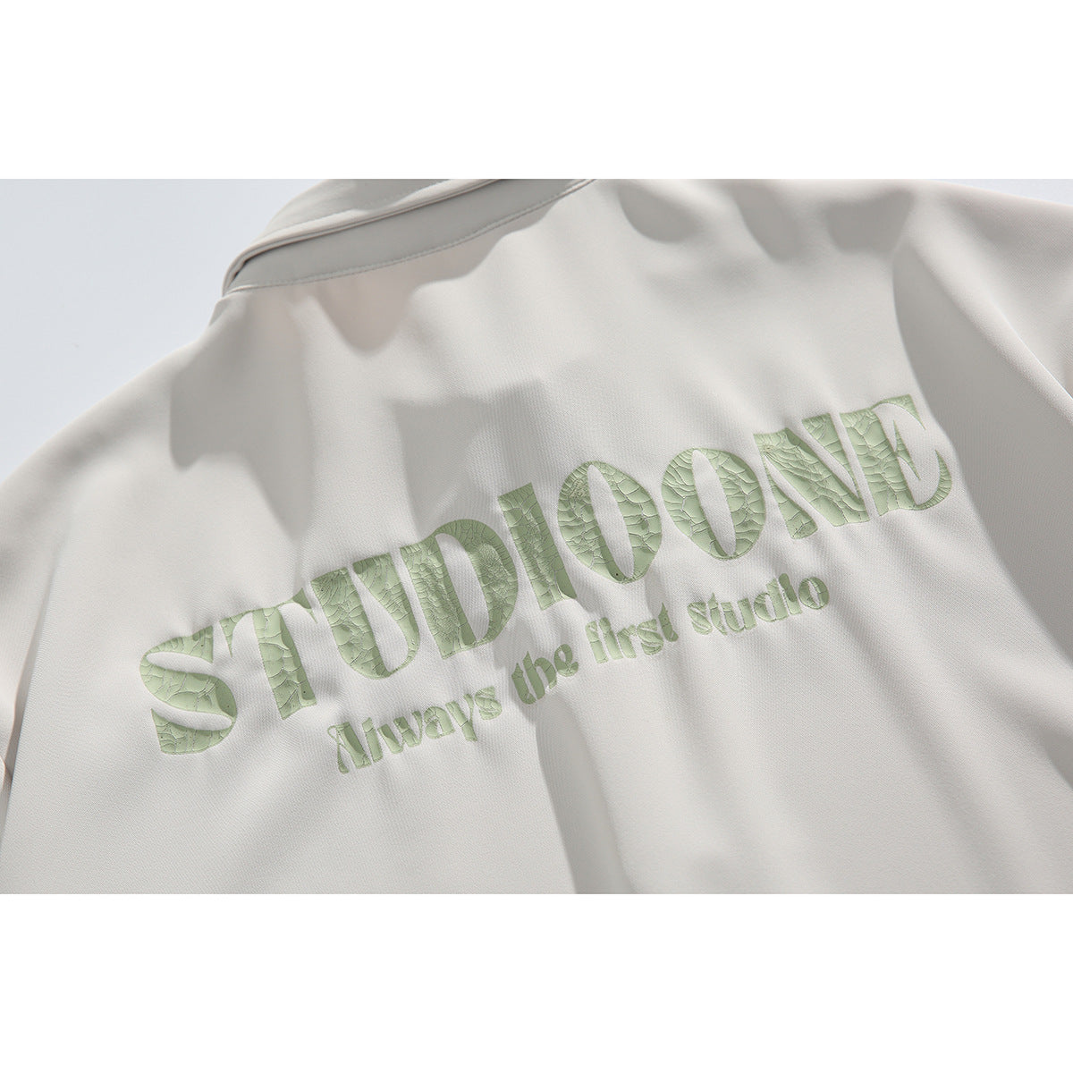 Close-up of pale green lettering on the back of an off-white shirt.