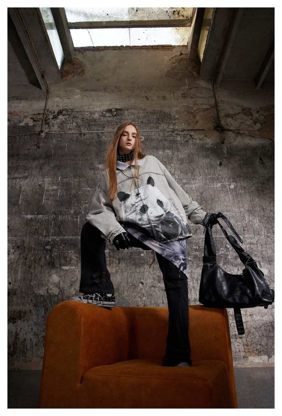 Model in gray panda-print denim-style jacket with black pants, posed with one foot on an orange chair