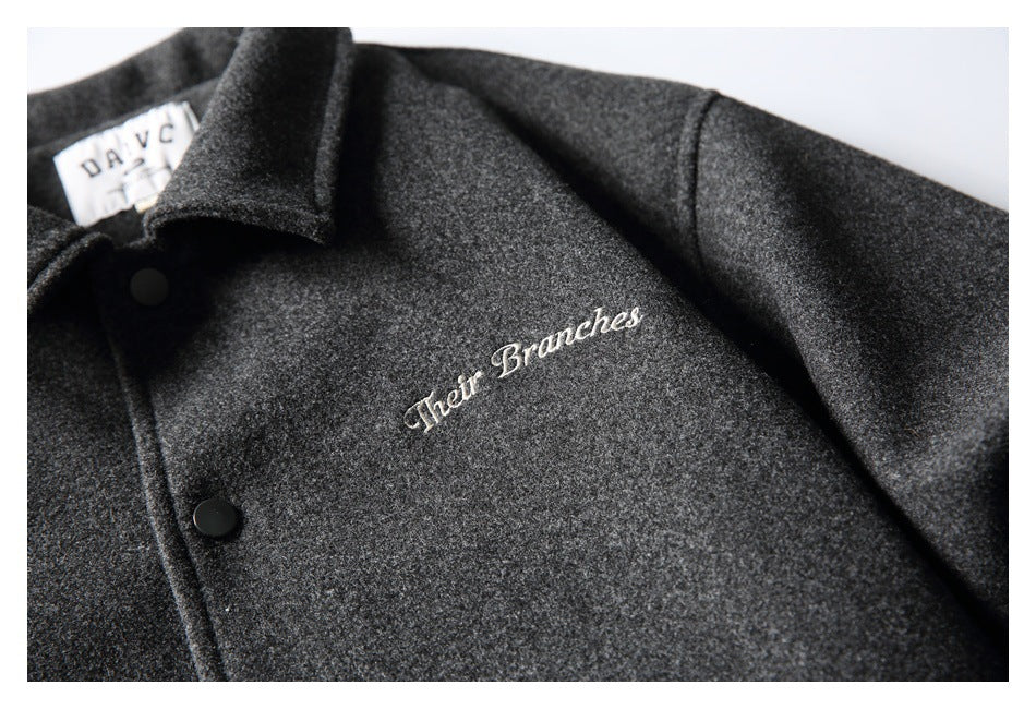 Close-up of cream script embroidery on the chest of a charcoal gray jacket, with part of its collar and snaps visible.