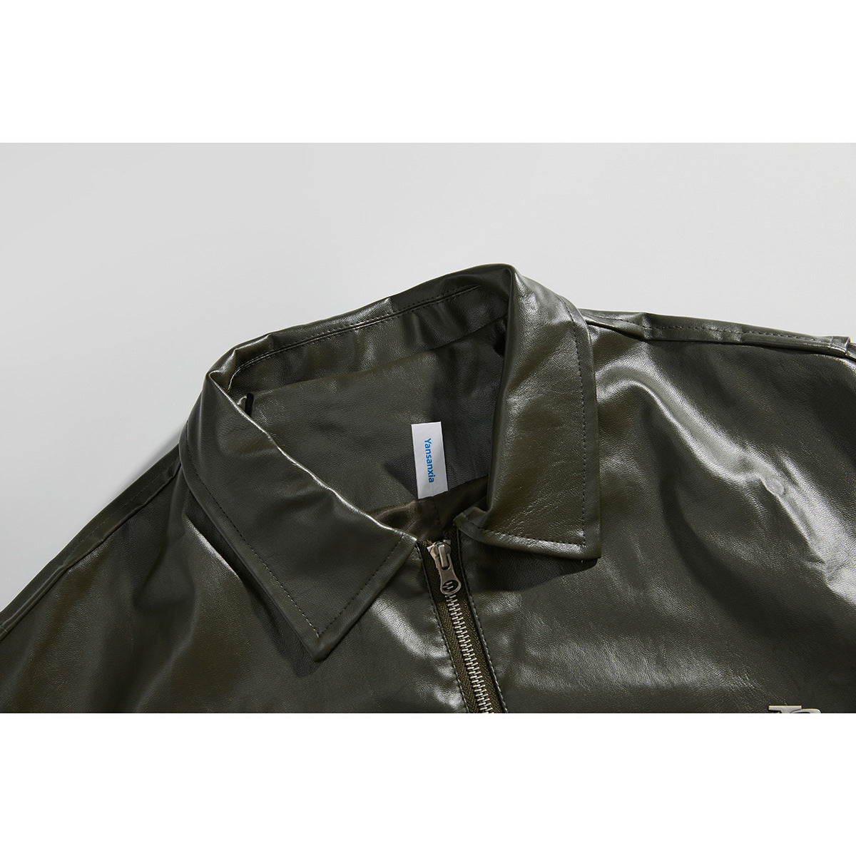Close-up of an olive jacket's pointed collar and front zipper, with a small neck label.
