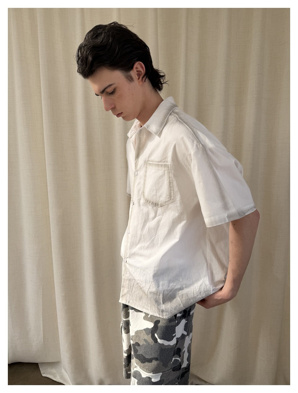 Model wearing a white short-sleeve button-up shirt with a chest pocket, shown from a side angle.