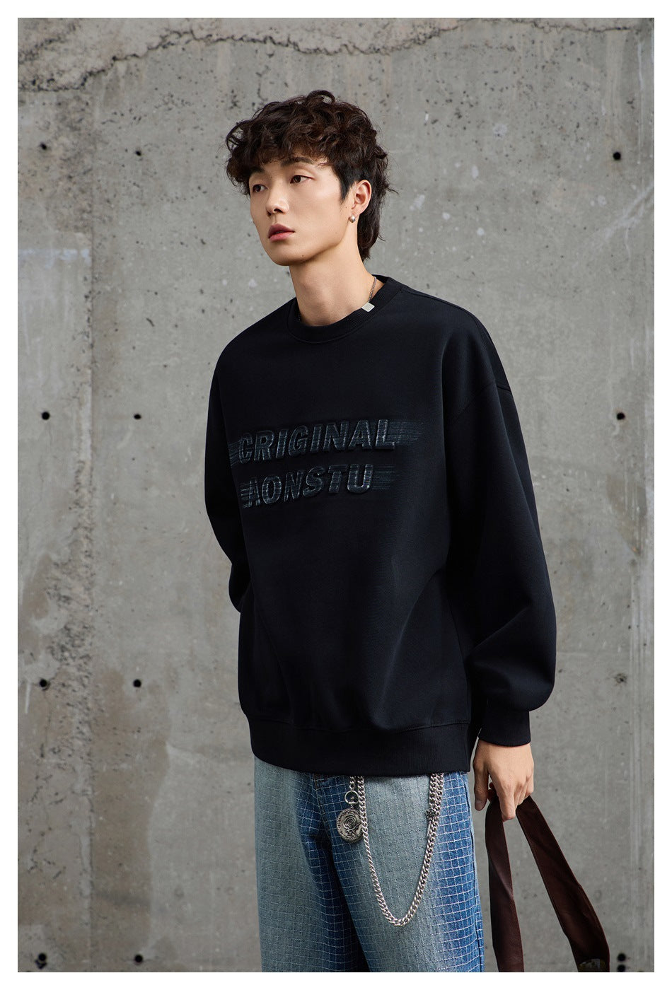 Model wearing a black crewneck sweatshirt with raised lettering and light blue patterned jeans.
