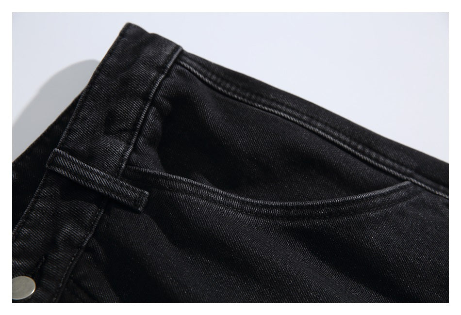 Close-up of black jeans showing a belt loop, waistband seam, pocket opening, and metal button.