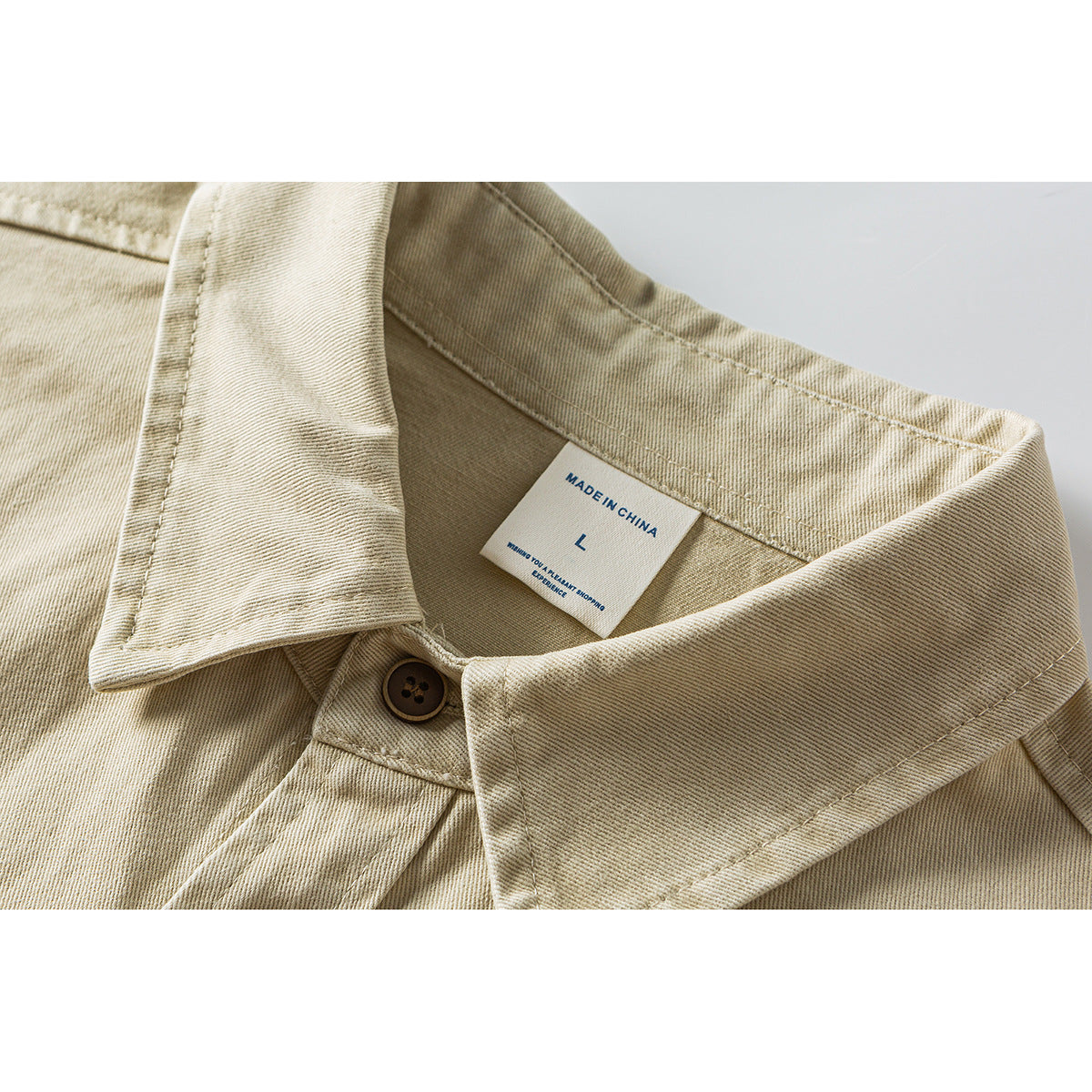 Close-up of a beige shirt collar, brown button, and neck label marked “Made in China” and size L.
