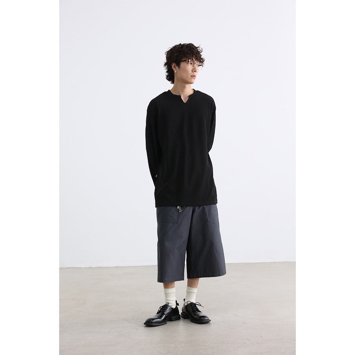 Model wearing a black long-sleeve shirt with a notched neckline and charcoal wide-leg shorts.