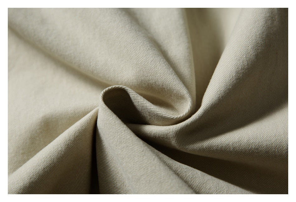 Macro view of beige garment fabric gathered into folds, showing its fine diagonal texture.