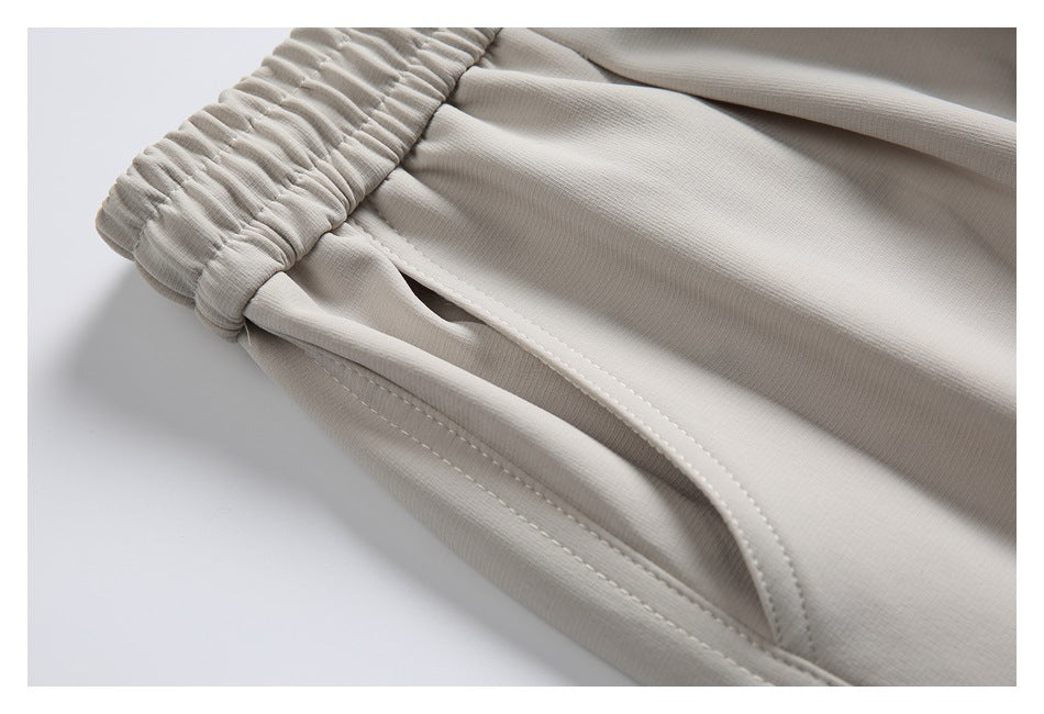 Close-up of the side pocket opening and stitching beneath the elastic waistband of light beige joggers.