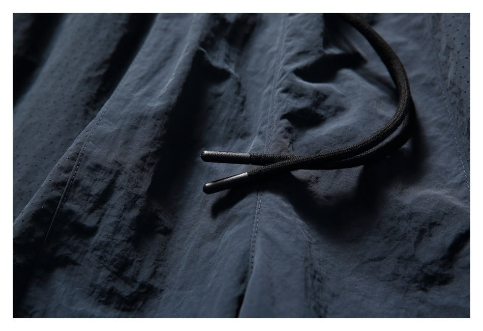 Close-up of black shorts showing a black drawcord, seams, and perforated fabric.