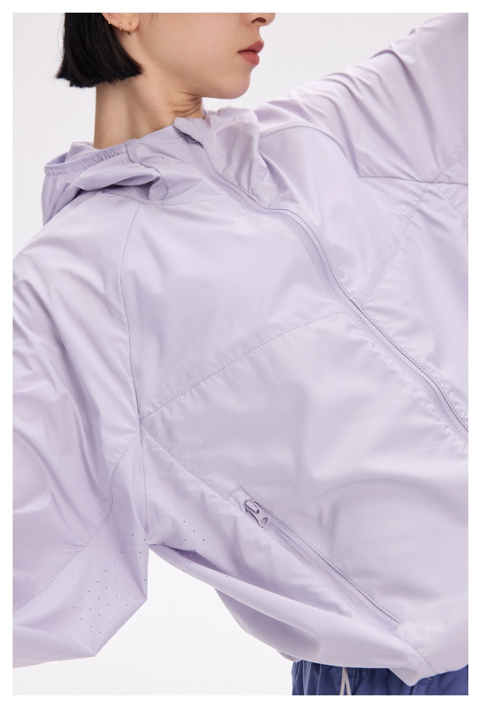 Close-up of a lavender hooded jacket showing its front zipper, panel seams, and small perforations near the sleeve.