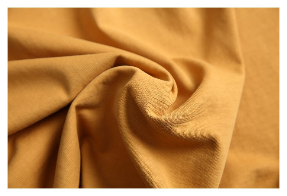 Close-up of mustard-gold shirt fabric twisted into folds, showing its surface texture.