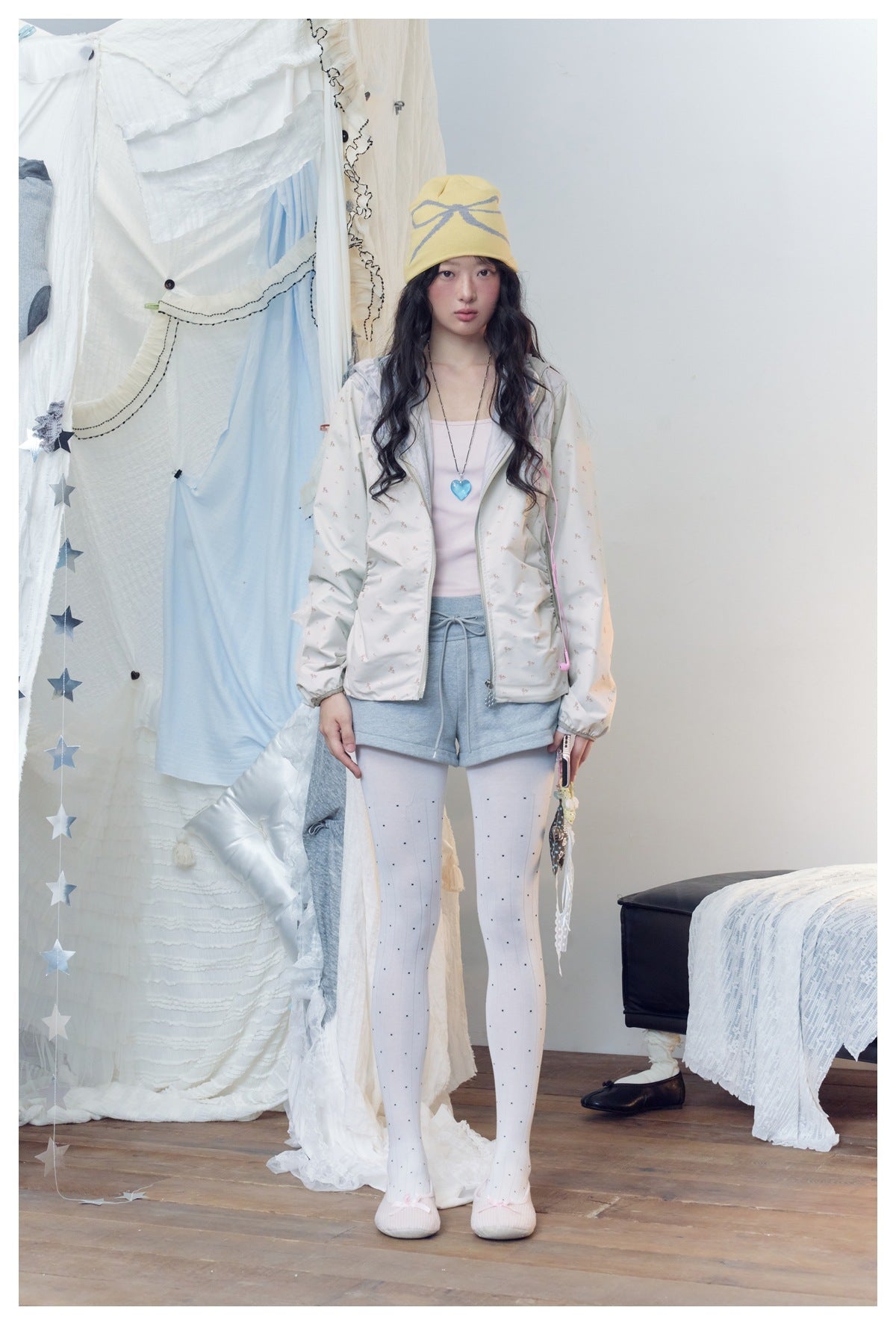 Model wearing a floral off-white hooded zip jacket with gray shorts, white polka-dot tights and a yellow bow beanie