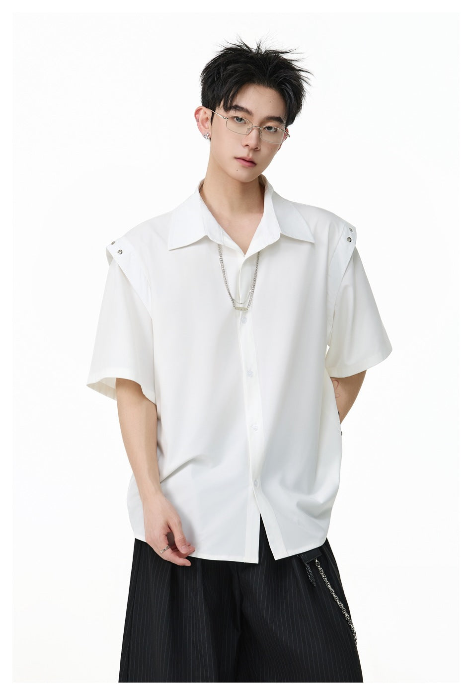 Close-up of a model in a white short-sleeve shirt with shoulder studs, a collar and a silver chain over the placket