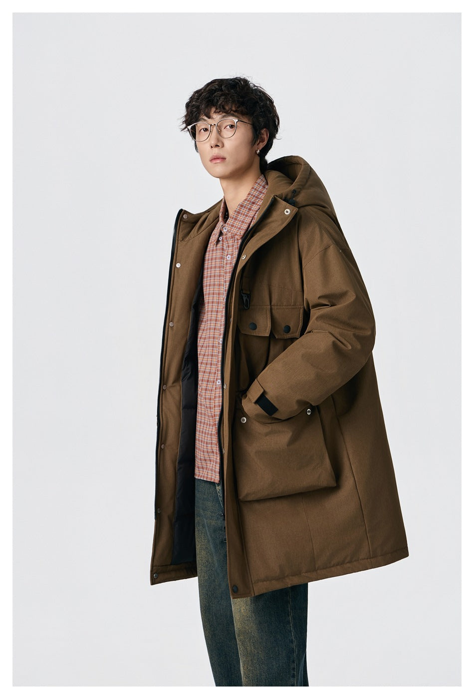 Close view of a model wearing an open brown hooded coat with large flap pockets over a plaid shirt.