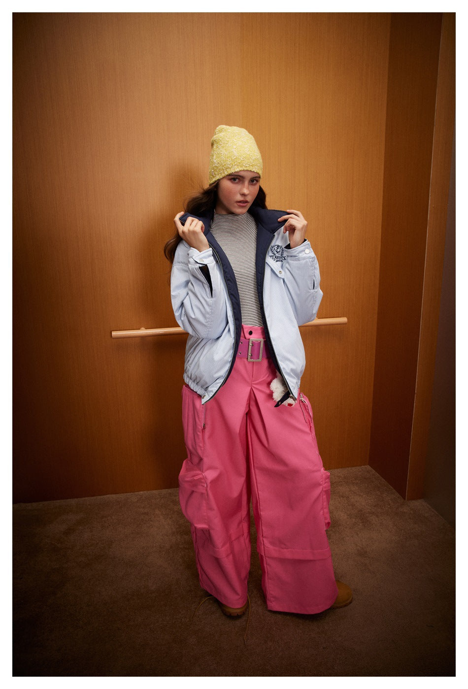Full-length model in a light blue pinstriped jacket, yellow beanie and wide-leg pink cargo trousers.