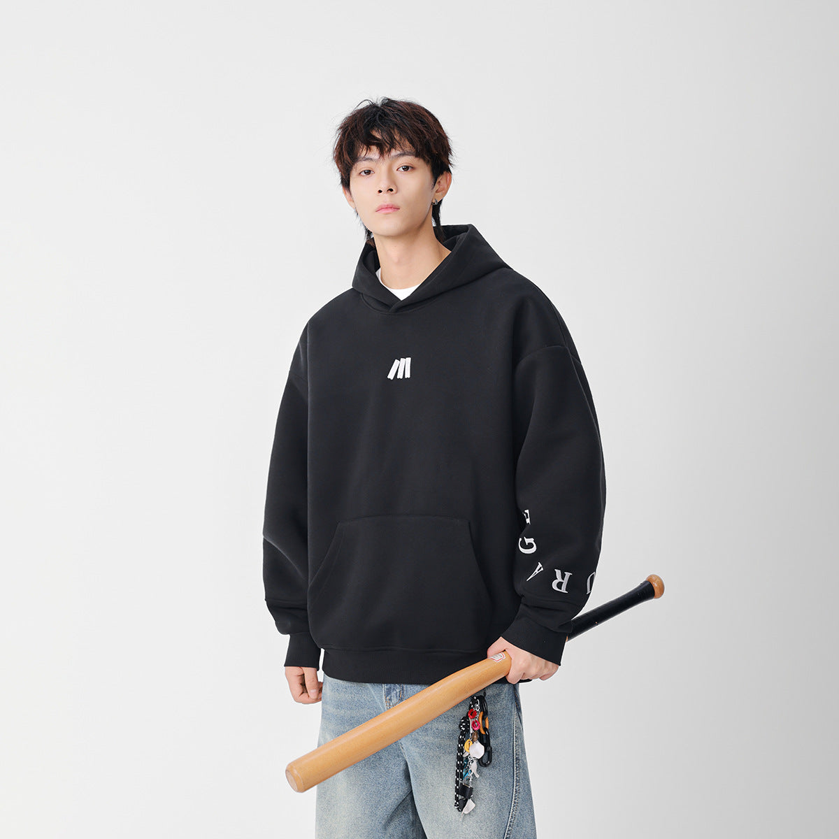 Model wearing a black oversized hoodie with a white chest emblem and sleeve lettering, paired with light-wash jeans.