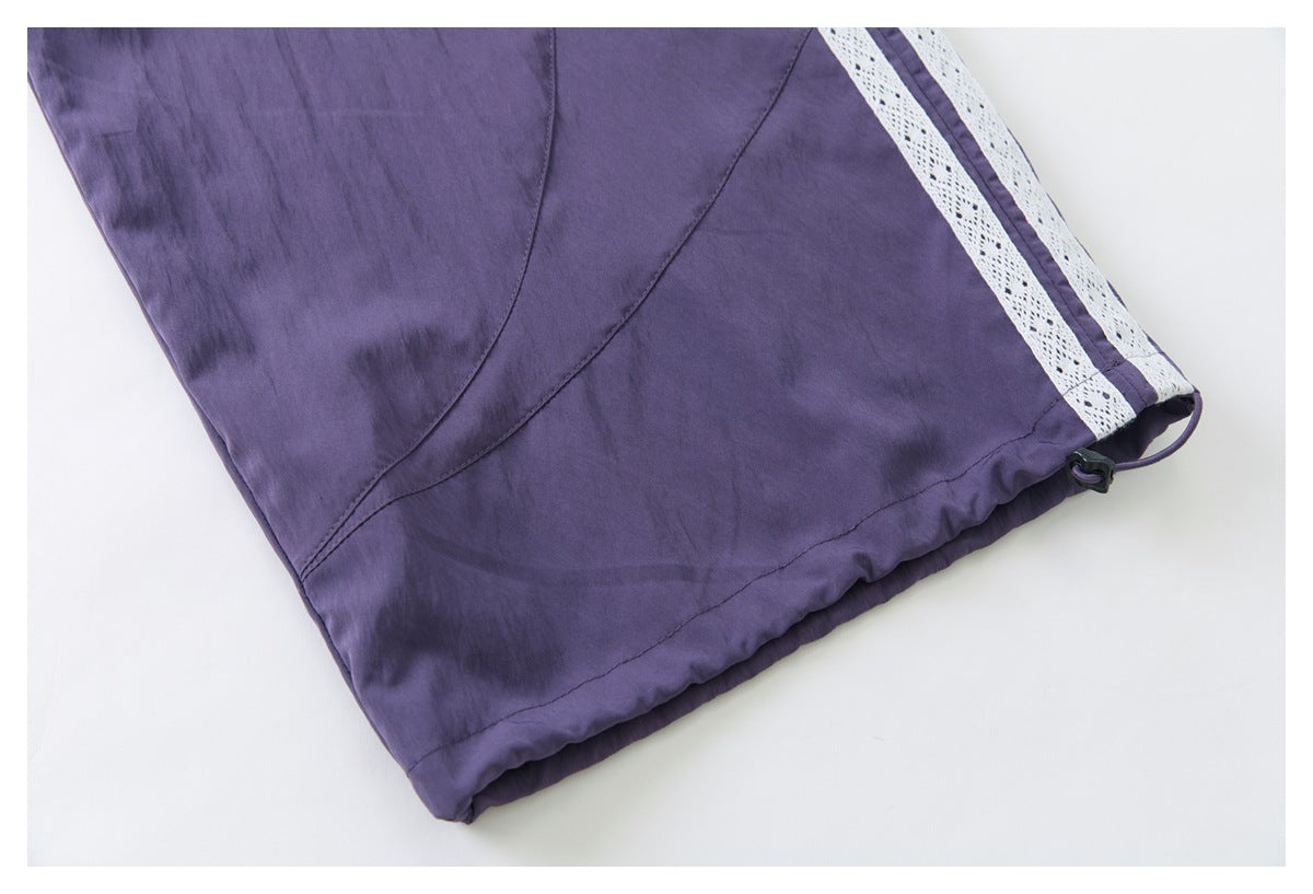 Close-up of a purple pants hem with a drawcord toggle and a white lace stripe along the side.