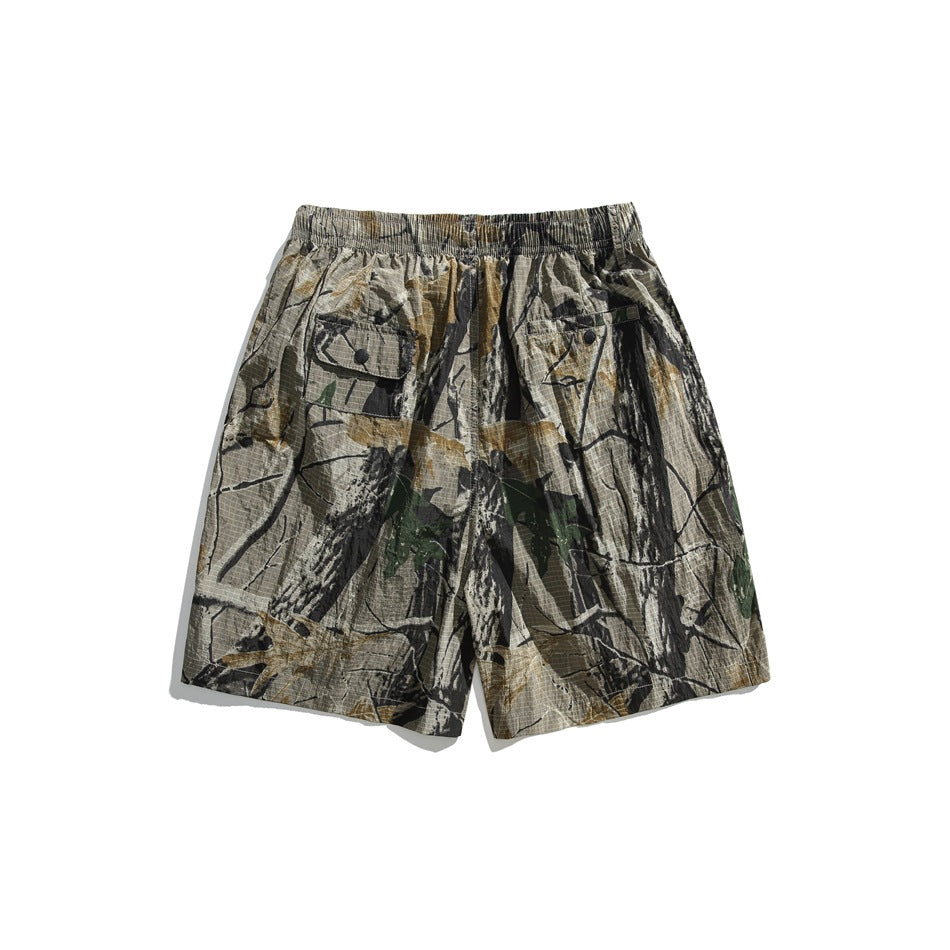 Front view of loose camouflage shorts with an elastic waist and two button-flap pockets.