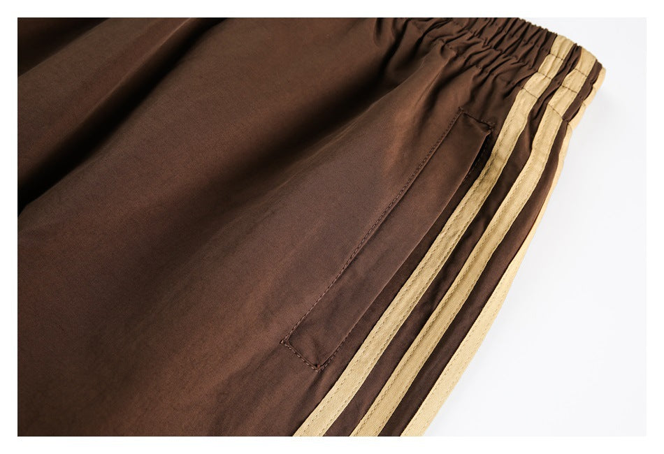 Close-up of brown track pants with a side pocket and three tan stripes along the leg.