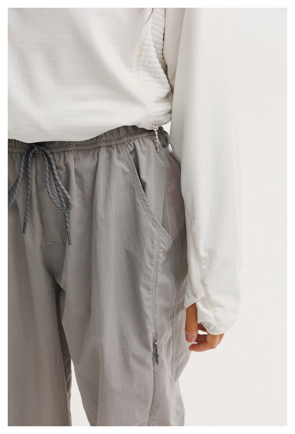 Close-up of gray pants showing the drawstring waist, slanted pocket, and small zippered detail.