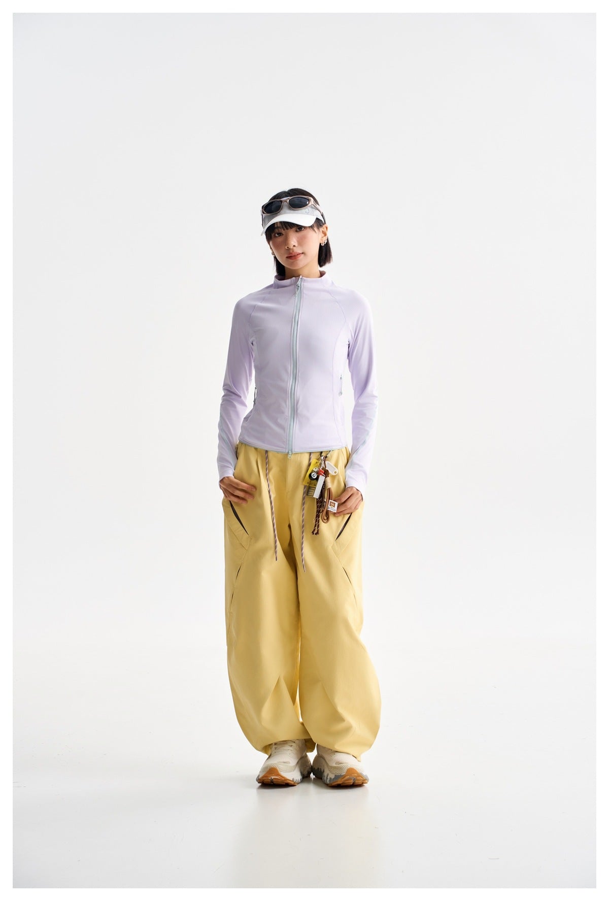 Model wearing a zipped pale lavender jacket and loose yellow trousers, viewed from the front.