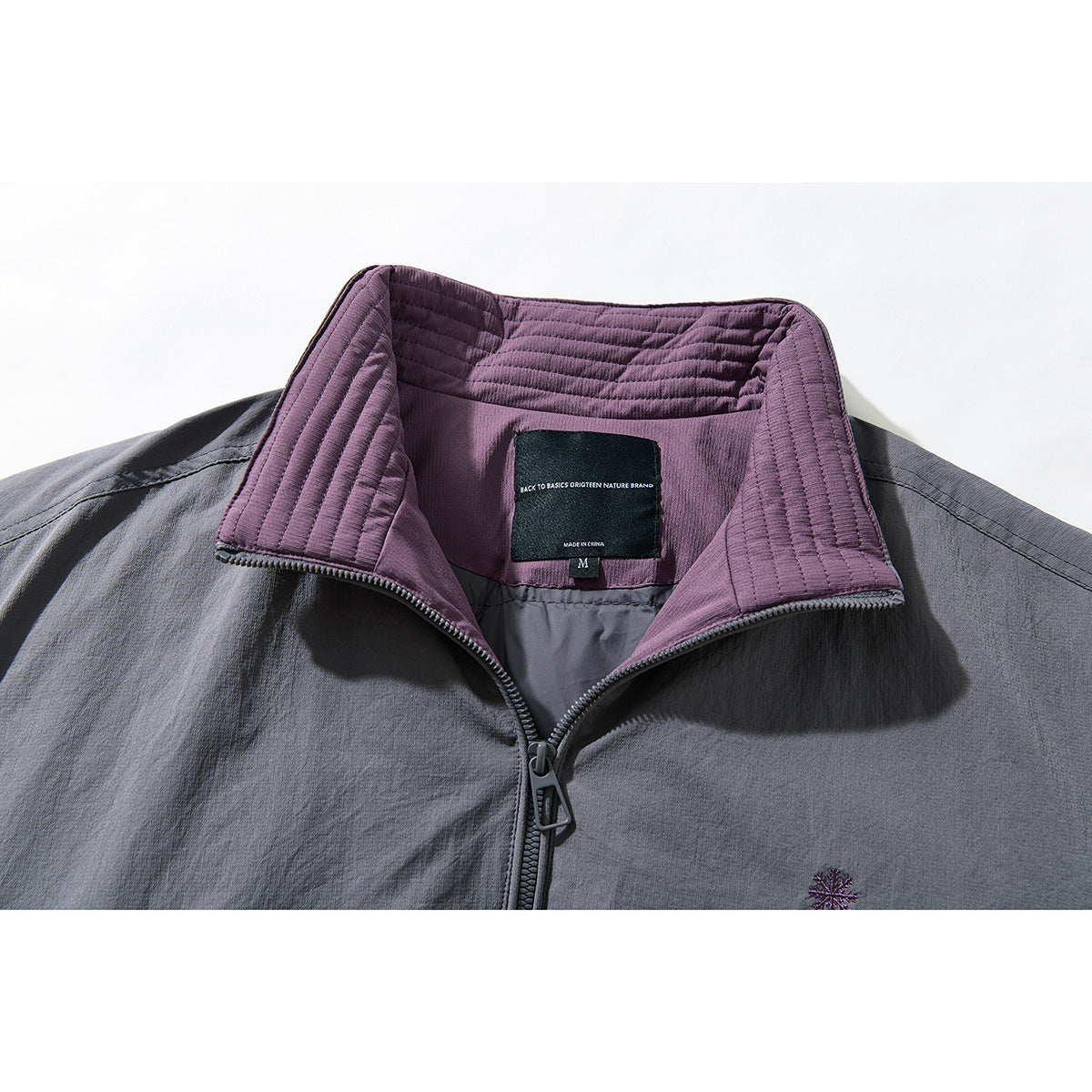Close-up of a gray jacket’s plum quilted stand collar, open zipper, and inner neck label.