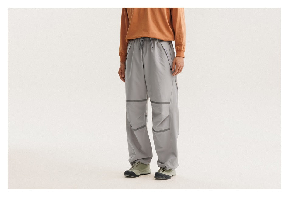 Rear three-quarter view of a person wearing loose gray drawstring pants with dark bands across the legs.