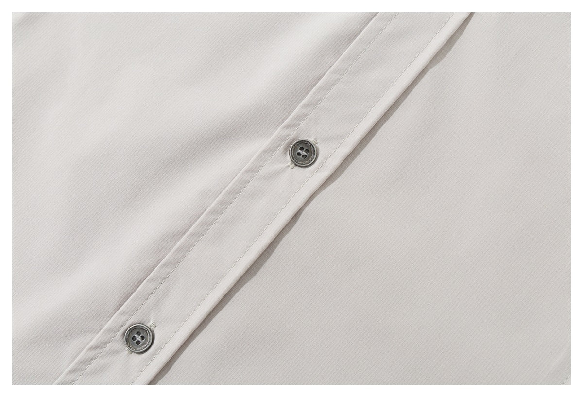 Close-up of two gray buttons on the light beige shirt's stitched front placket.