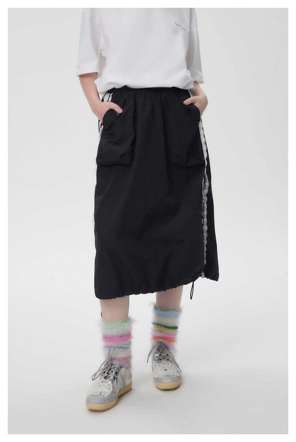 Model wearing the black midi skirt in front view with hands in the flap pockets and lace-trimmed sides
