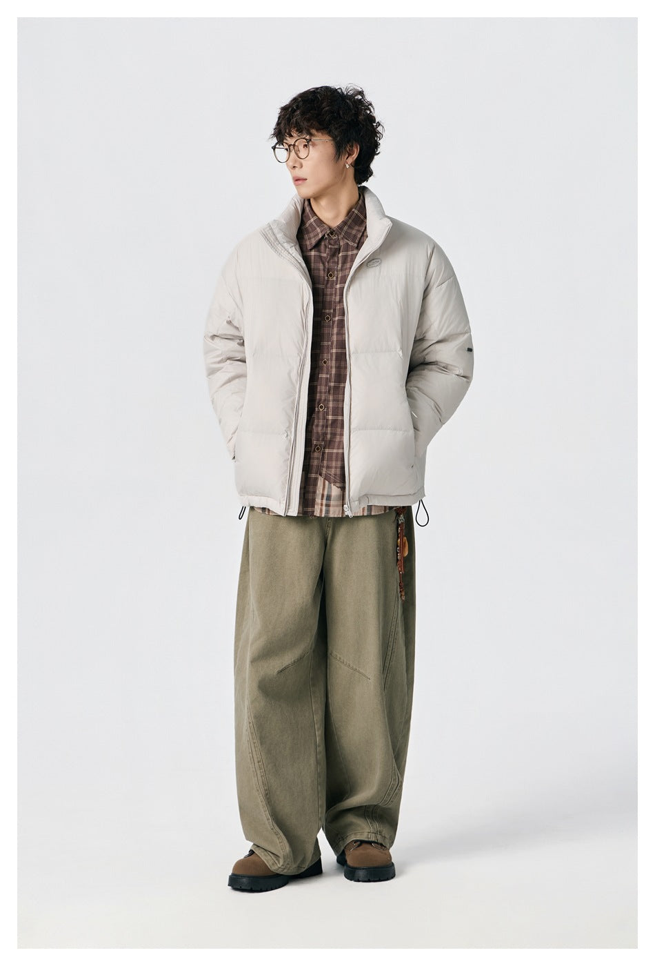 Full-length view of a model wearing an off-white puffer jacket with drawcord hem and wide olive trousers.